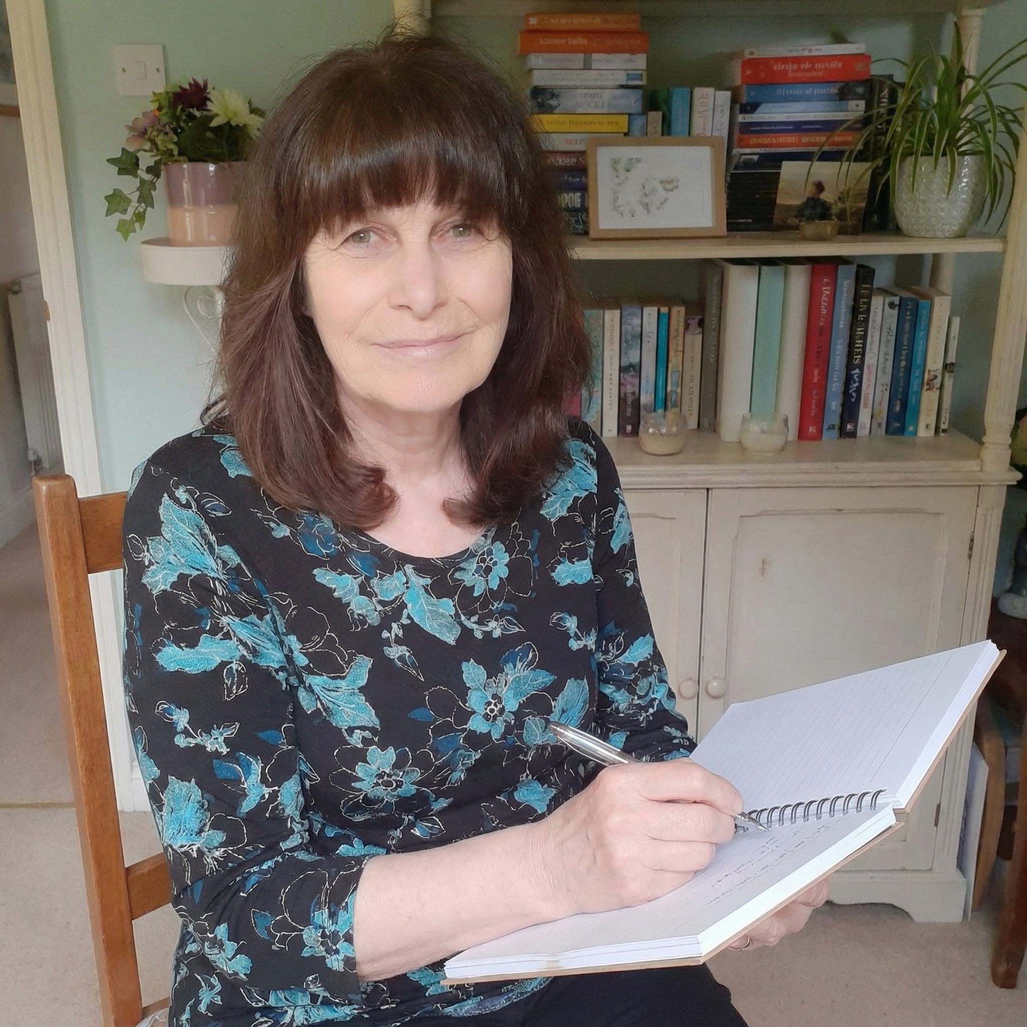 Author Susie Sharp sitting with a notebook and pen in front of bookshelves, working on her next novel.